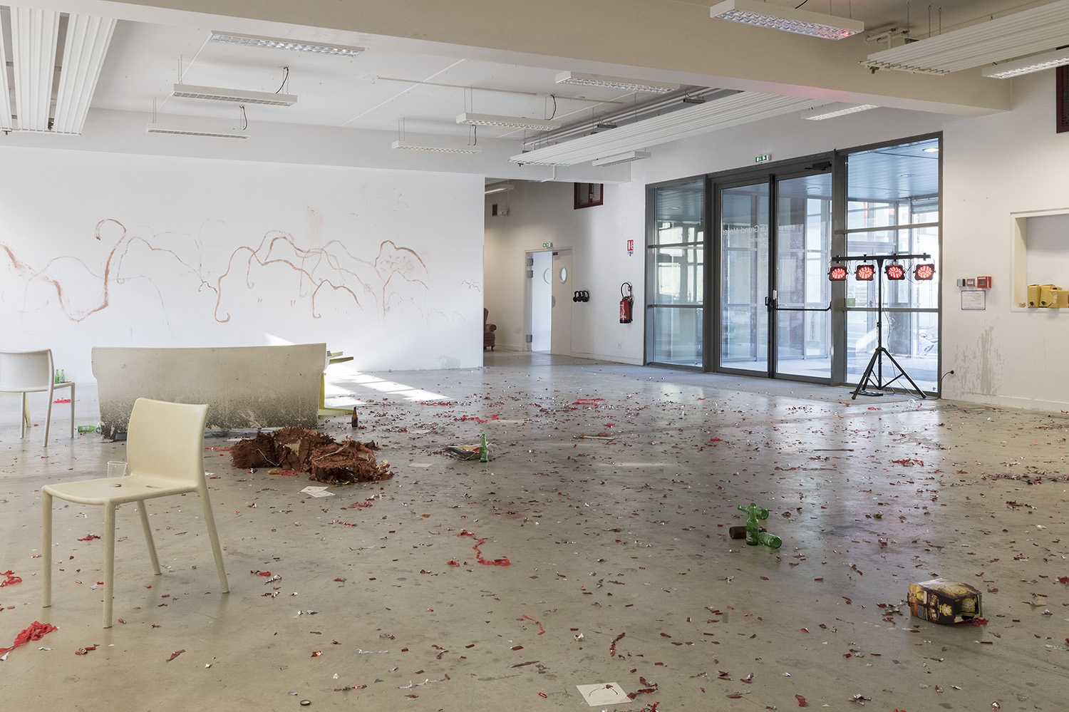 photo du lendemain : les murs sont recouerts de dessins de mammouth mais il y a aussi un soleil. le piñata est en morceaux par terre, les cotillons sont partout, des bouteilles de bières jonchent le sol, un canapé et des chaises sont au milieu de tout ça. Un spot de 4 lmières est en marche.